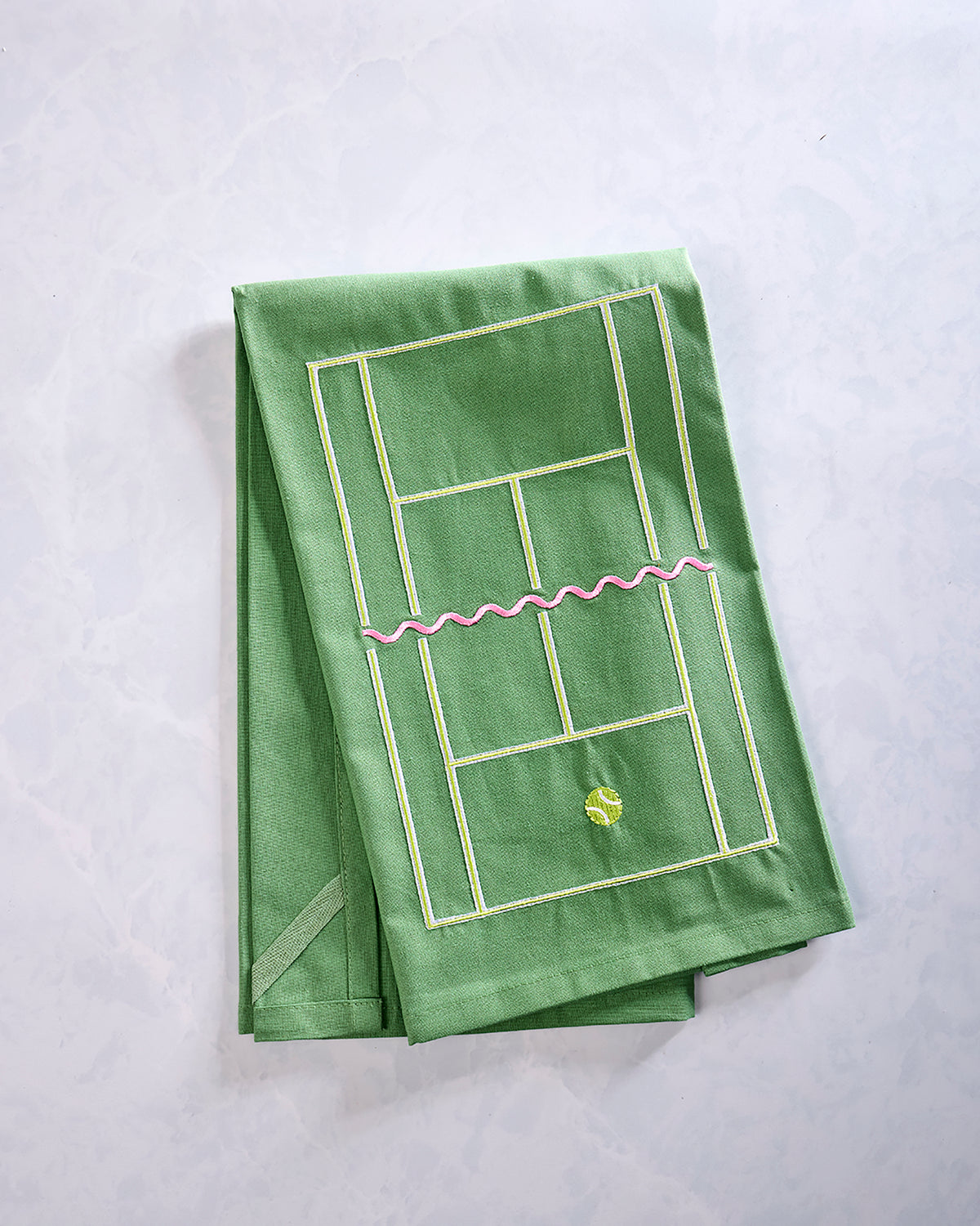 Green tea towel embroidered with a tennis-court design, pink net, and small tennis ball motif, folded on a light background.