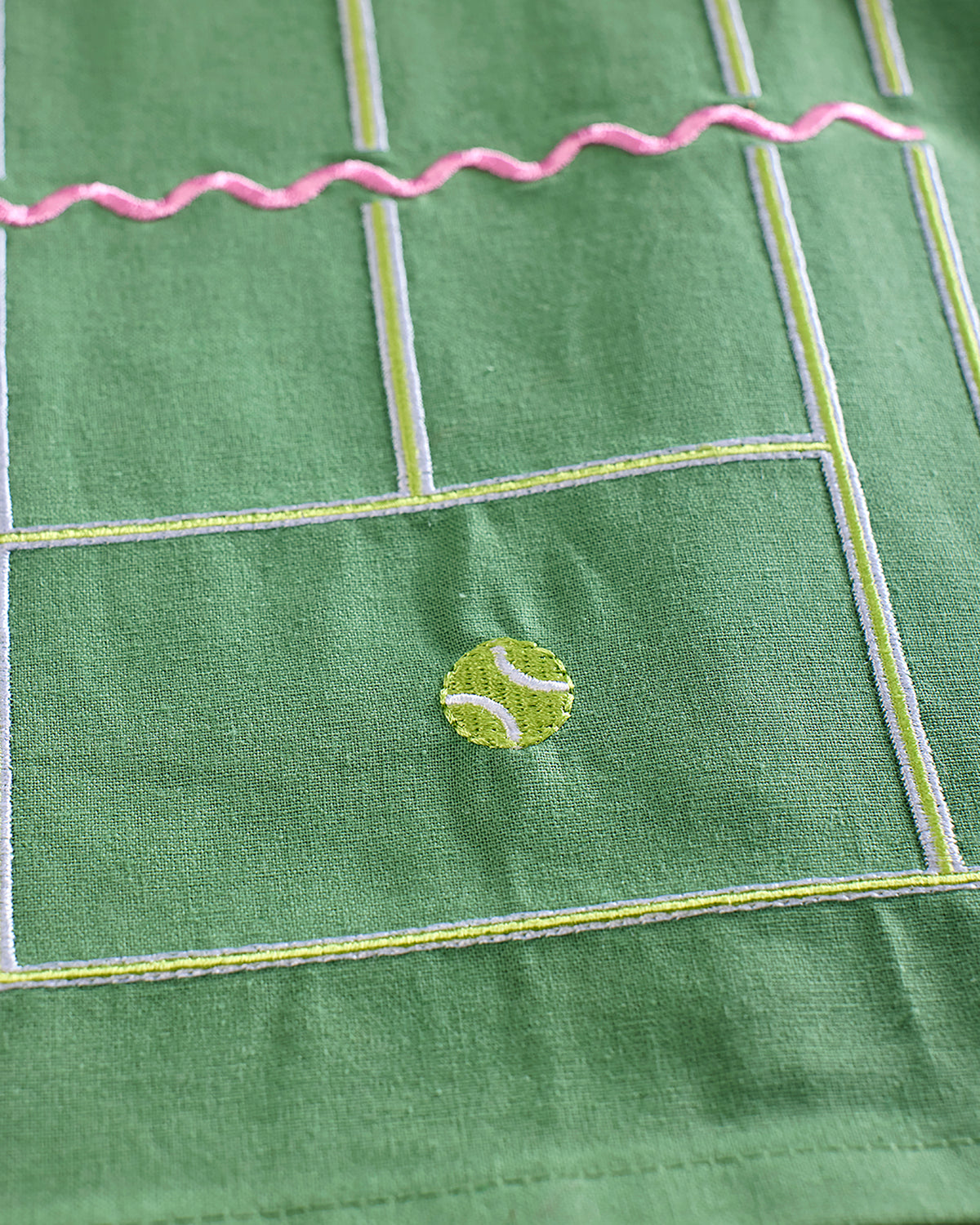 Close-up of a green tennis-court tea towel showing the pink net detail and embroidered tennis ball motif.