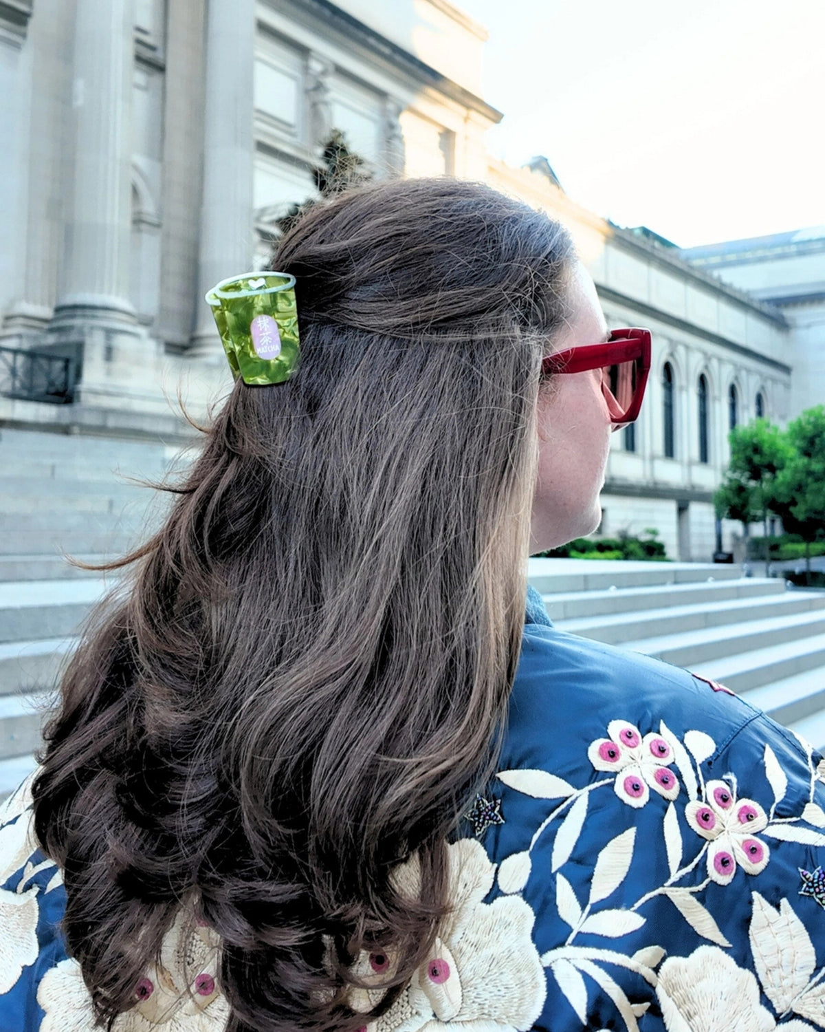 Green matcha-cup claw hair clip securing a section of hair, viewed from behind outdoors.
