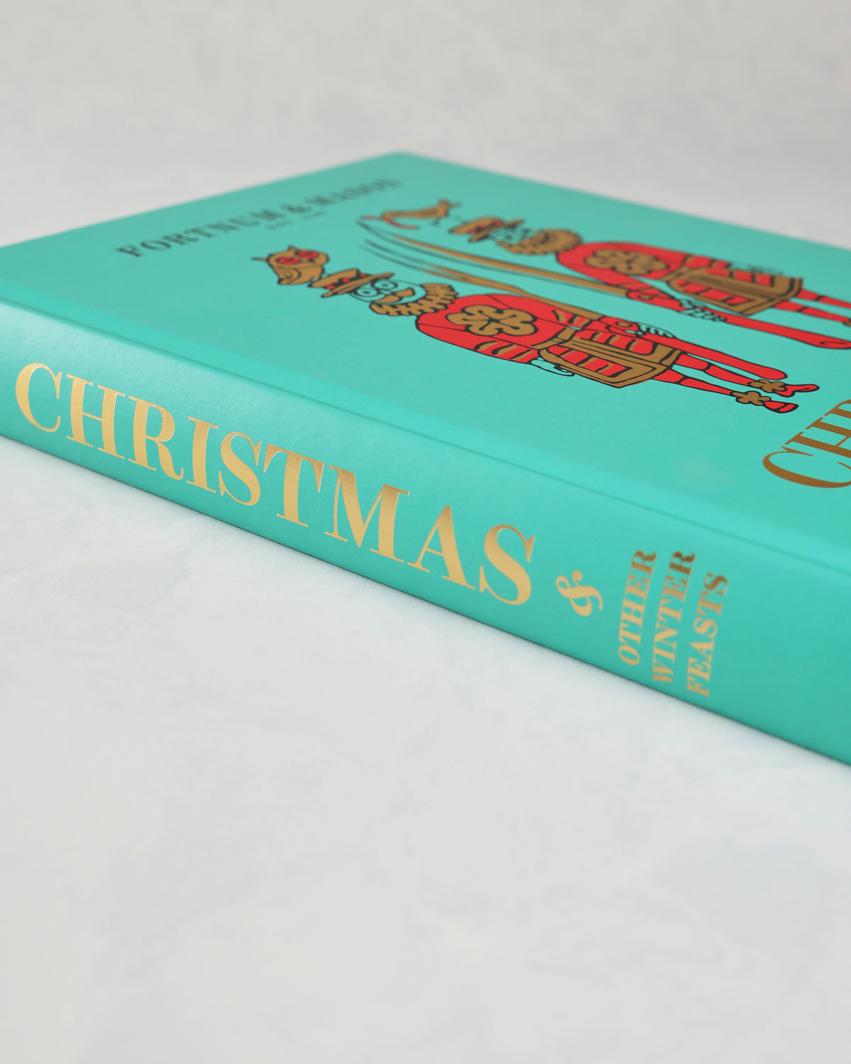 Angled view of the teal Fortnum & Mason Christmas & Other Winter Feasts book showing its gold-lettered spine.
