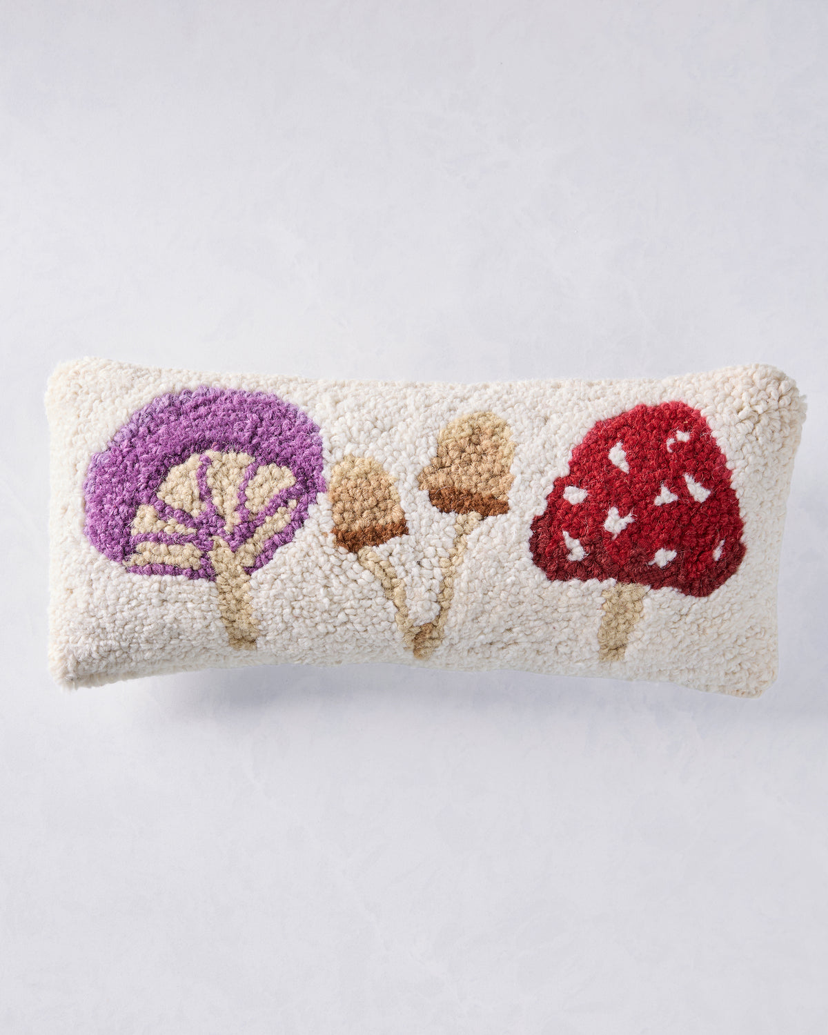 Front view of an ivory pillow decorated with purple, tan, and red mushrooms.