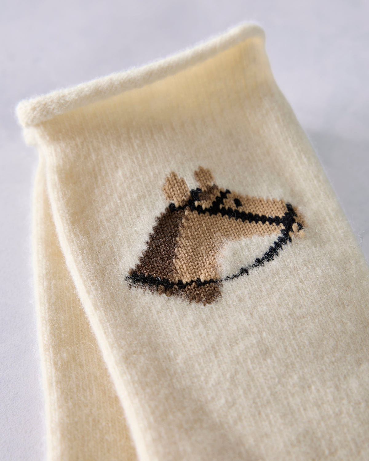 Close-up of a horse head embroidered on an ivory crew sock.