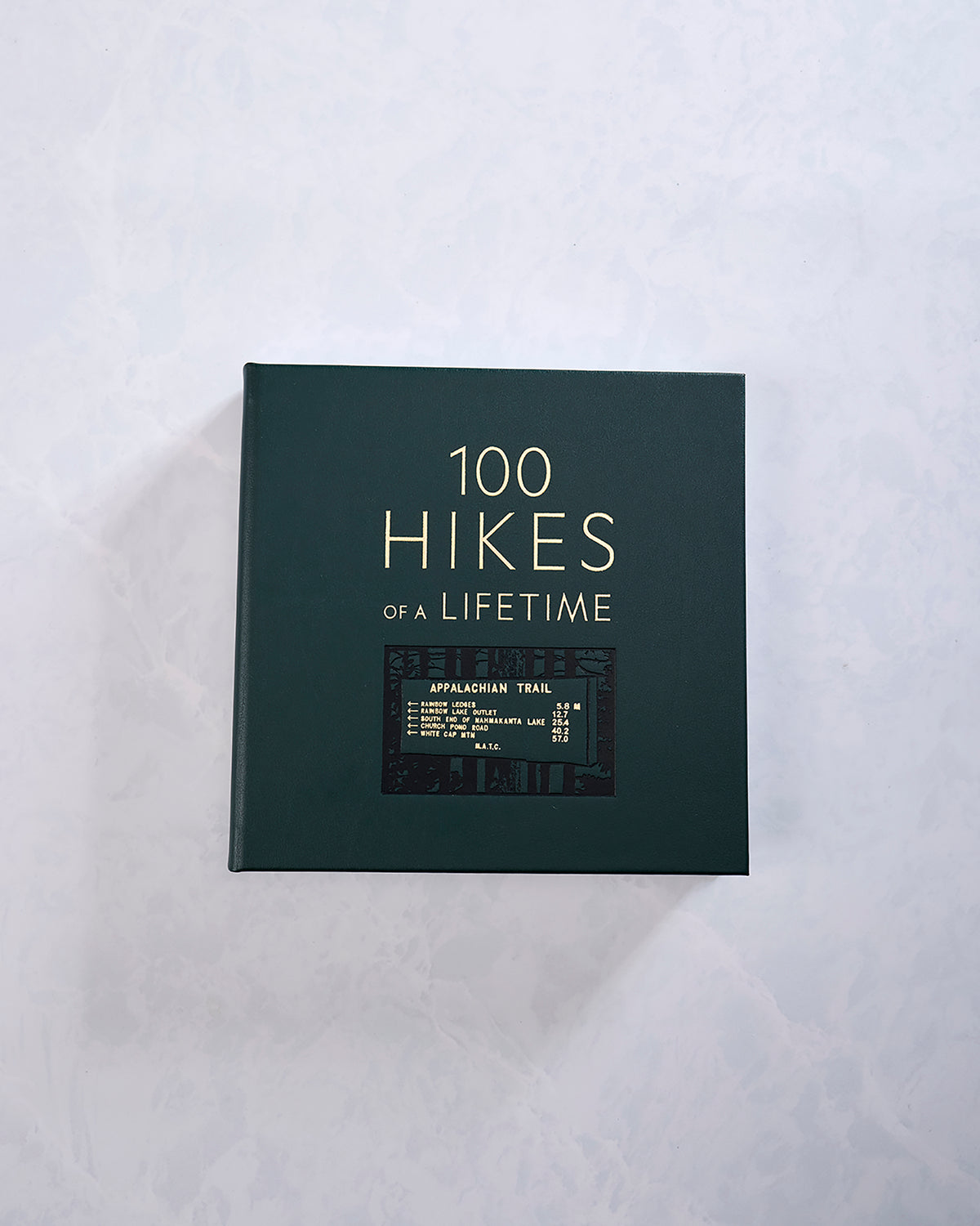 Hunter green hardcover book titled “100 Hikes of a Lifetime,” shown from the front with an Appalachian Trail sign graphic.