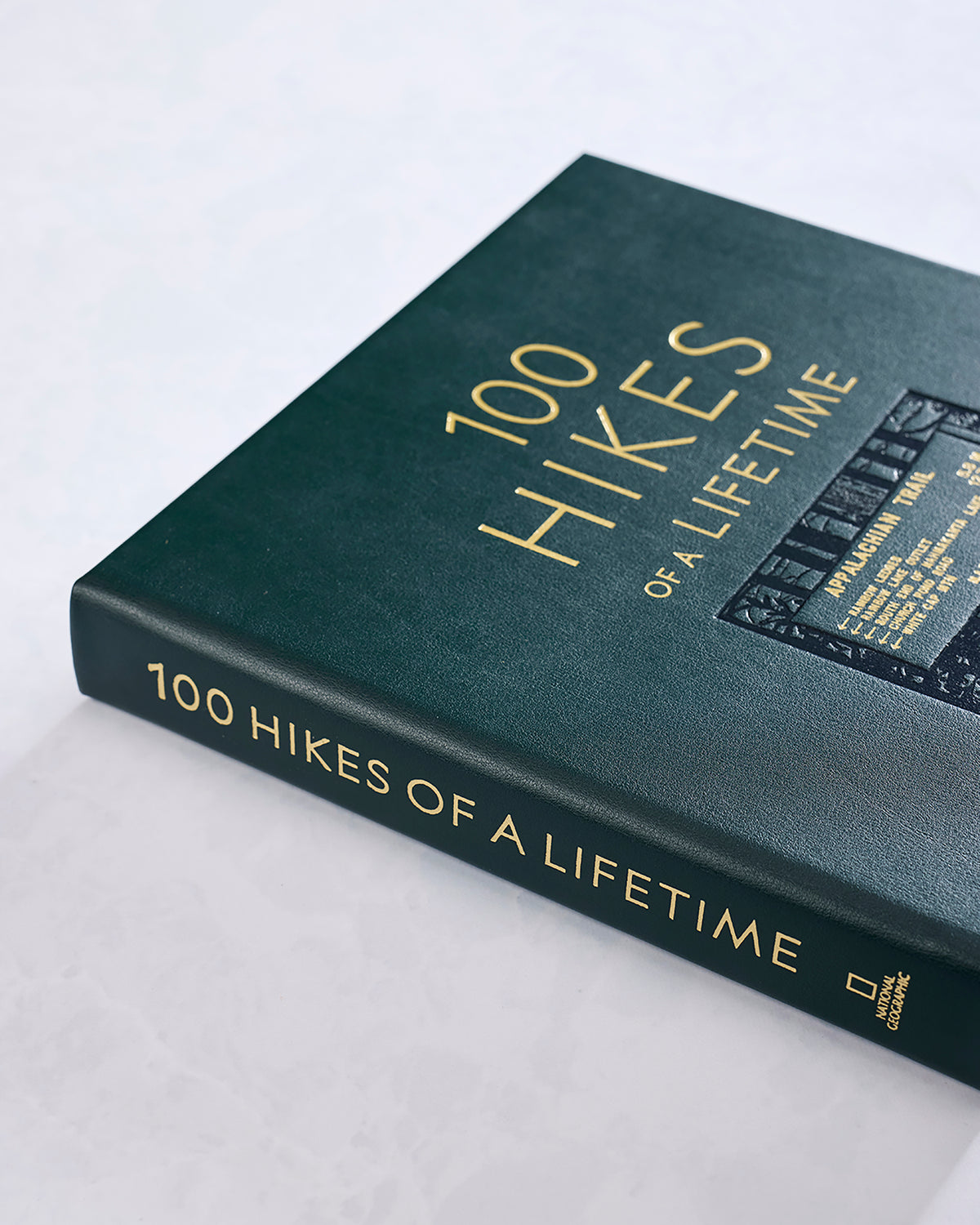 Close angled view of the hunter green hardcover book, showing the gold title on the cover and spine.