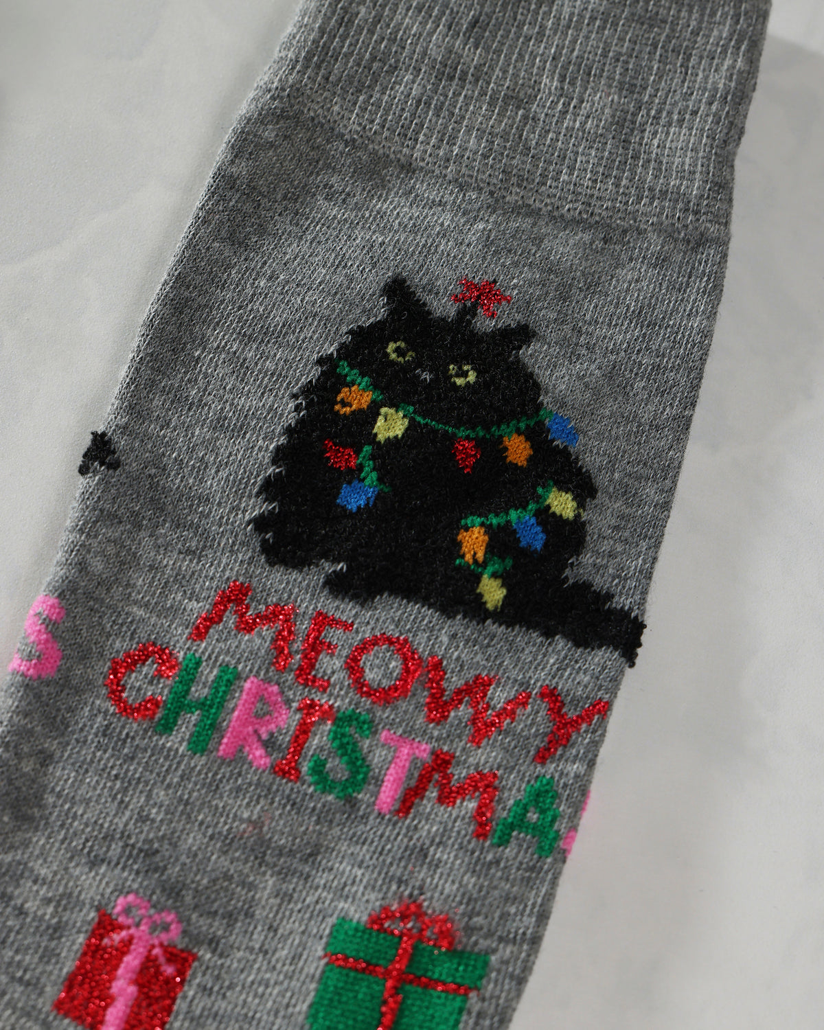 Close-up of a gray sock showing an embroidered black cat with Christmas lights and festive lettering