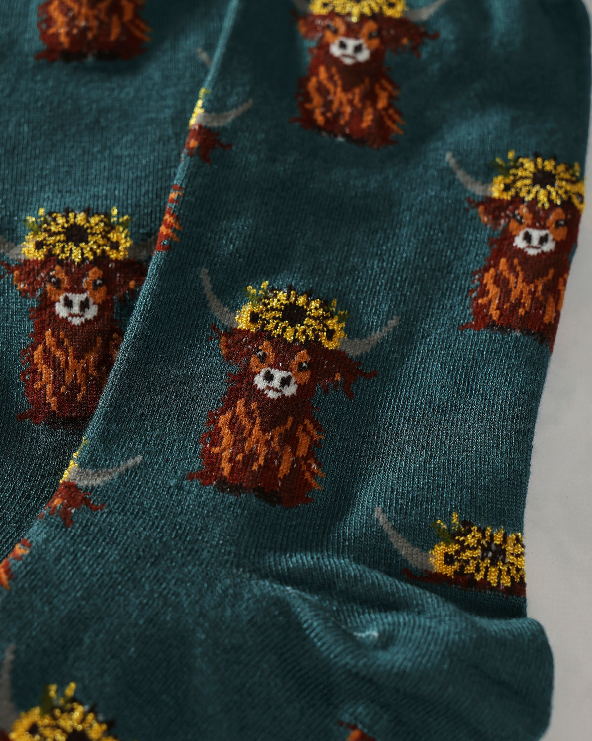 Close-up of the teal sock fabric and repeating Highland cow pattern, including flower crowns and horns.