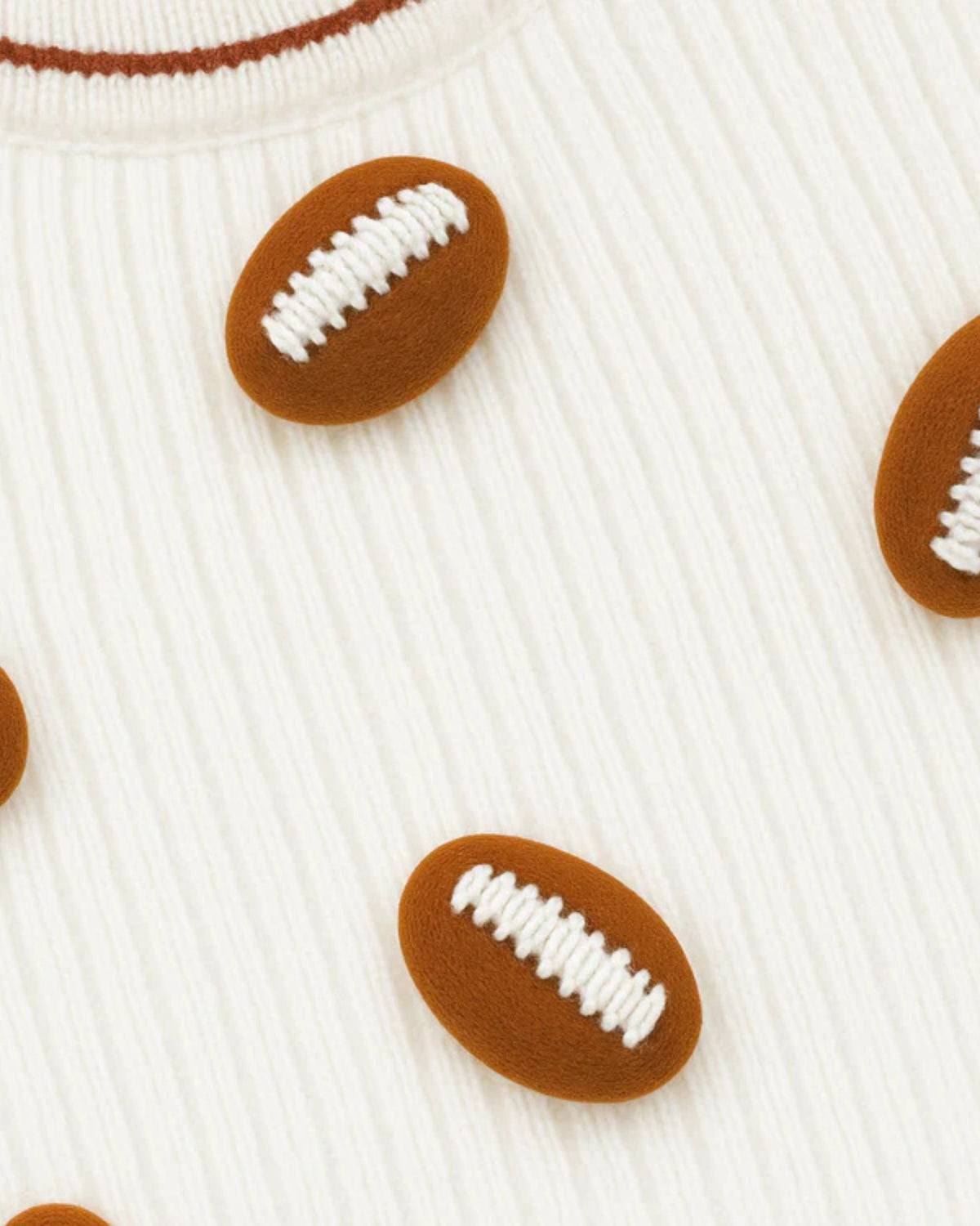 Close-up of brown football appliqués with white laces on an ivory sweater