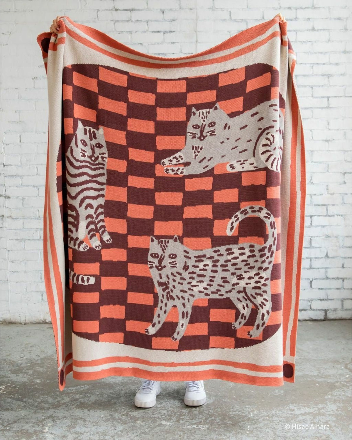 Three Cats knit throw blanket displayed vertically, showing three cats on an orange-and-brown checkerboard design.