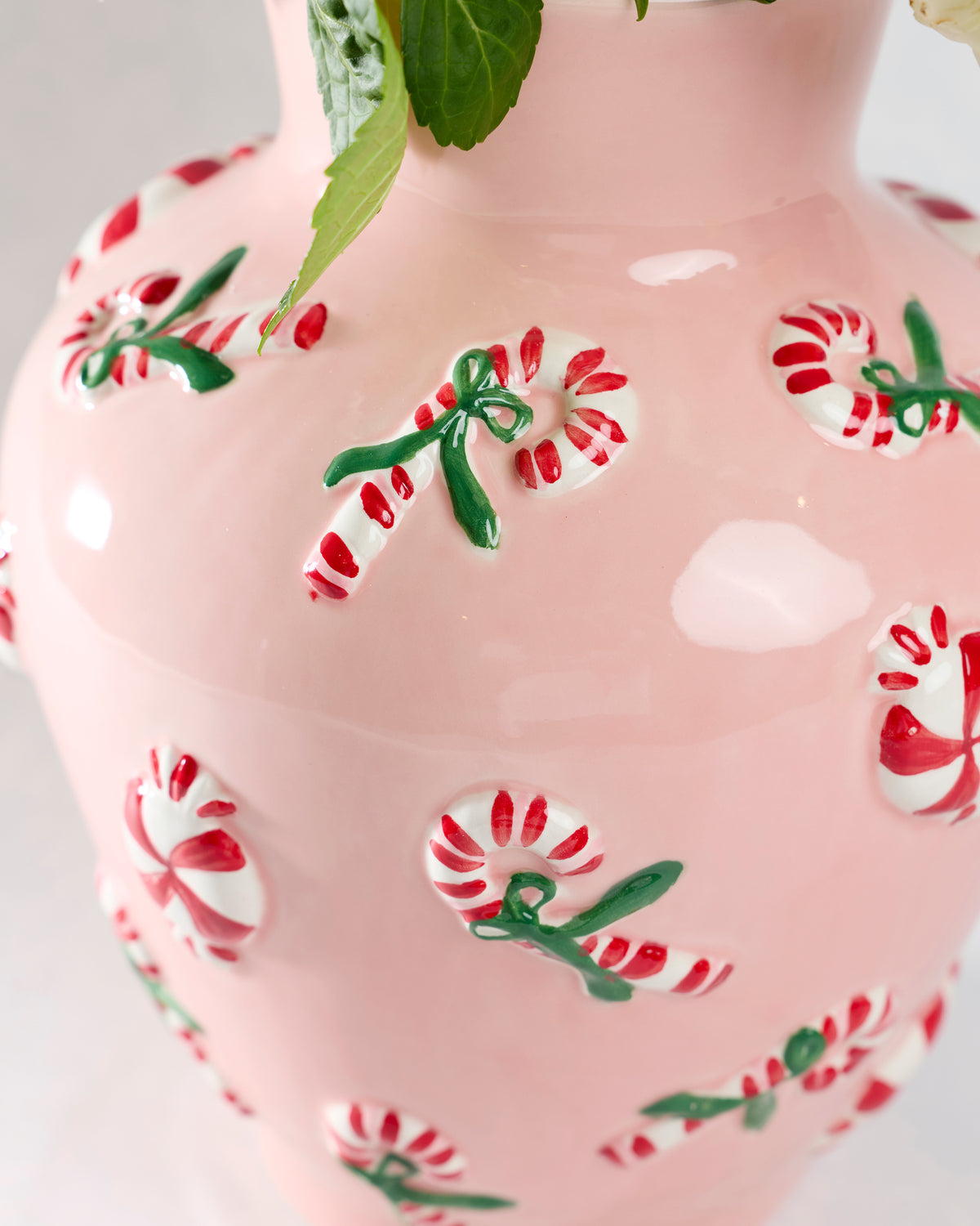 Close-up of the pink ceramic vase showing raised red-and-green peppermint details on its glossy surface.