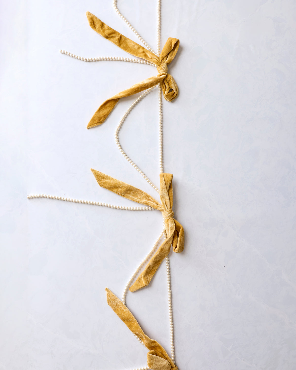 Gold bow garland with multiple velvet bows and faux pearl strands arranged vertically.
