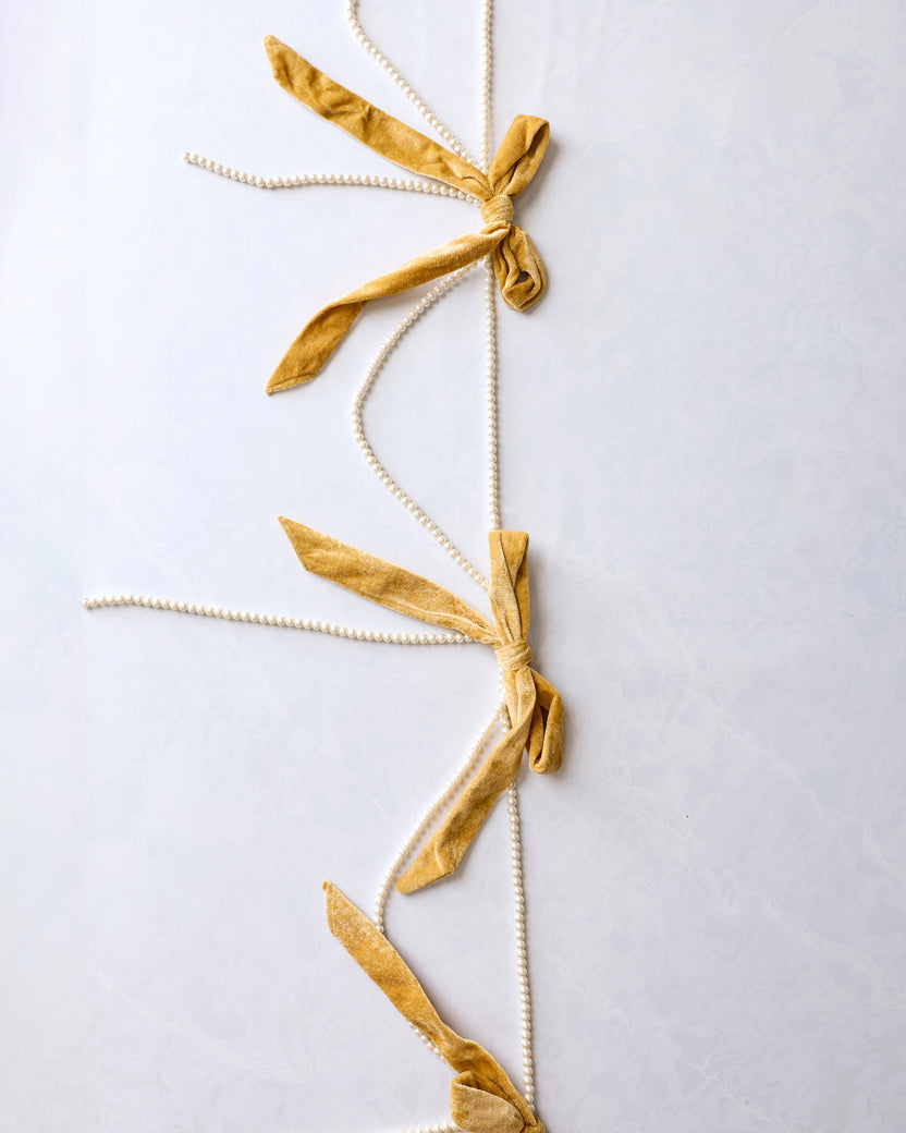 Gold bow garland with multiple velvet bows and faux pearl strands arranged vertically.