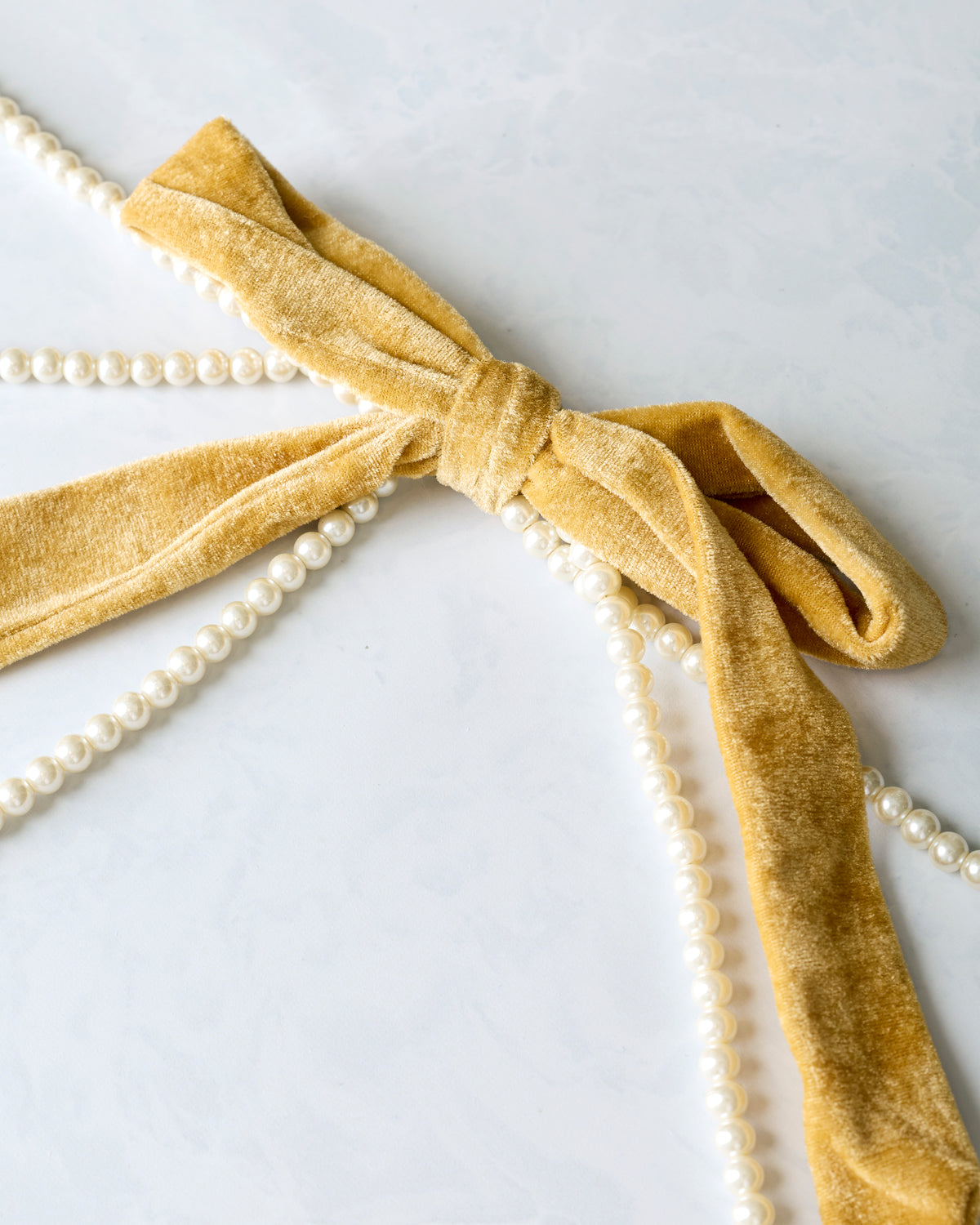 Close-up of a gold velvet bow tied around faux pearl strands on the garland.