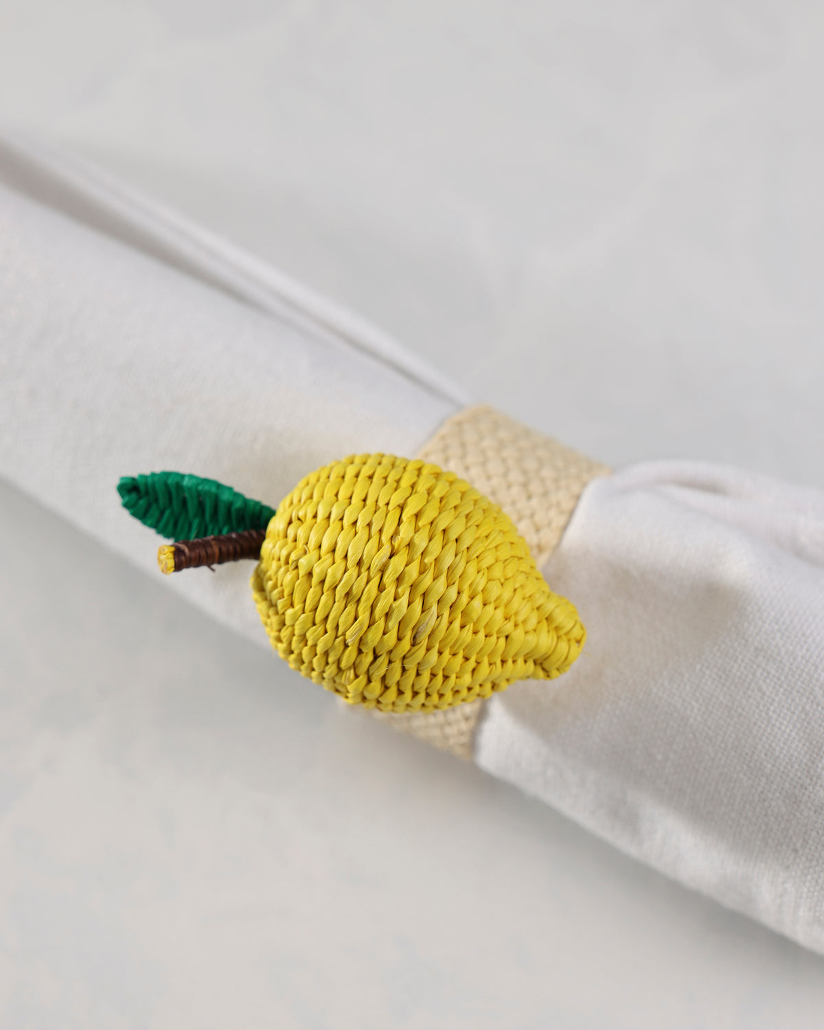 Close view of the yellow woven lemon napkin ring around a rolled white napkin.