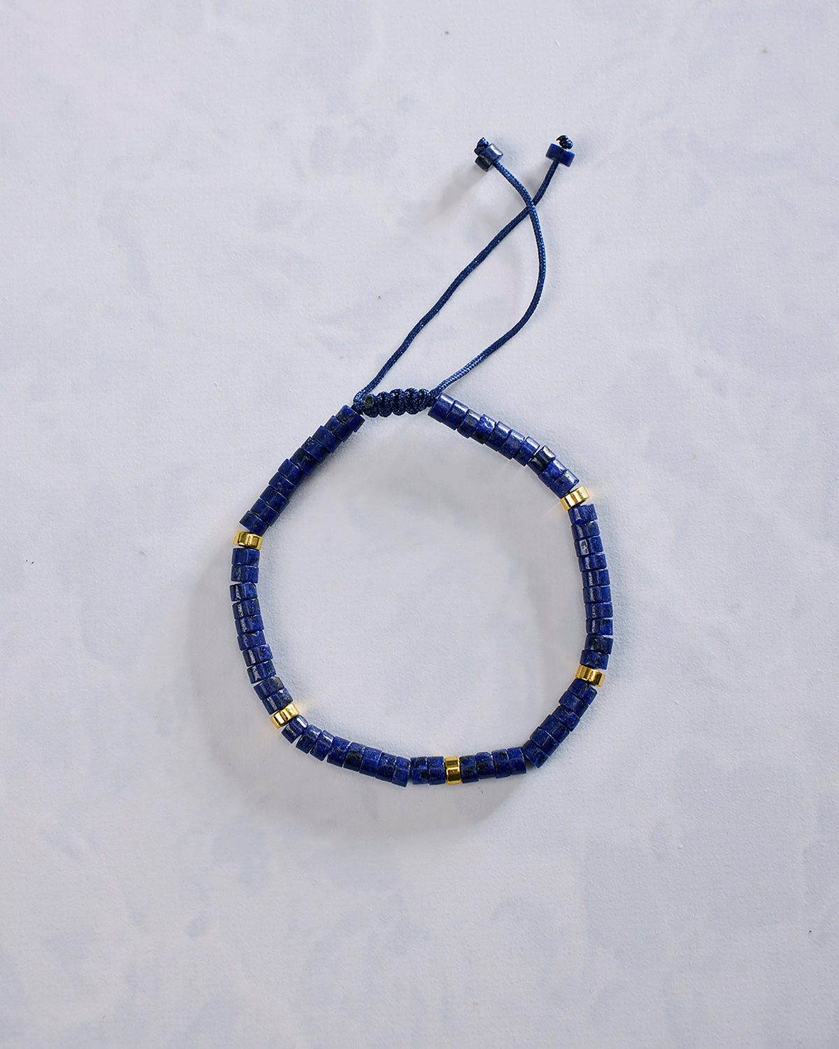 Blue beaded bracelet arranged in an oval, with small gold-tone accent beads and an adjustable cord closure.