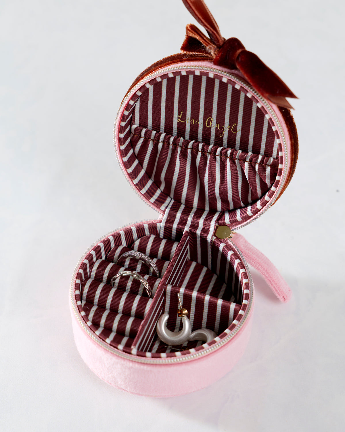 Open pink round jewelry case showing striped lining, ring rolls, compartments, and jewelry storage.