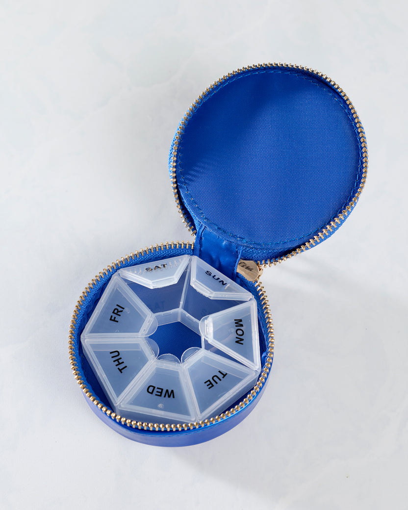 Open blue round pill case containing a removable seven-compartment organizer labeled for each day of the week.