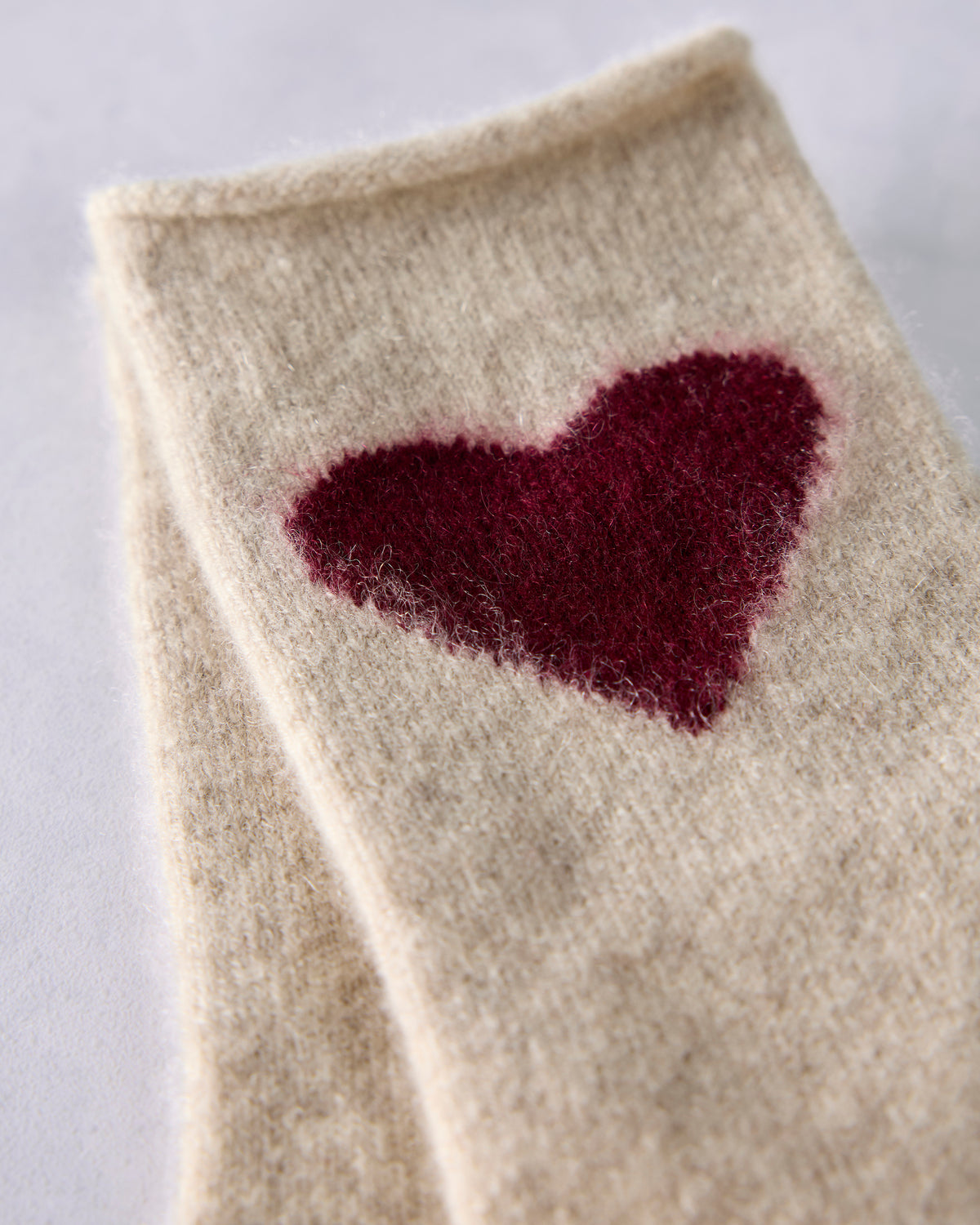 Close-up of a cream crew sock with a burgundy heart motif.