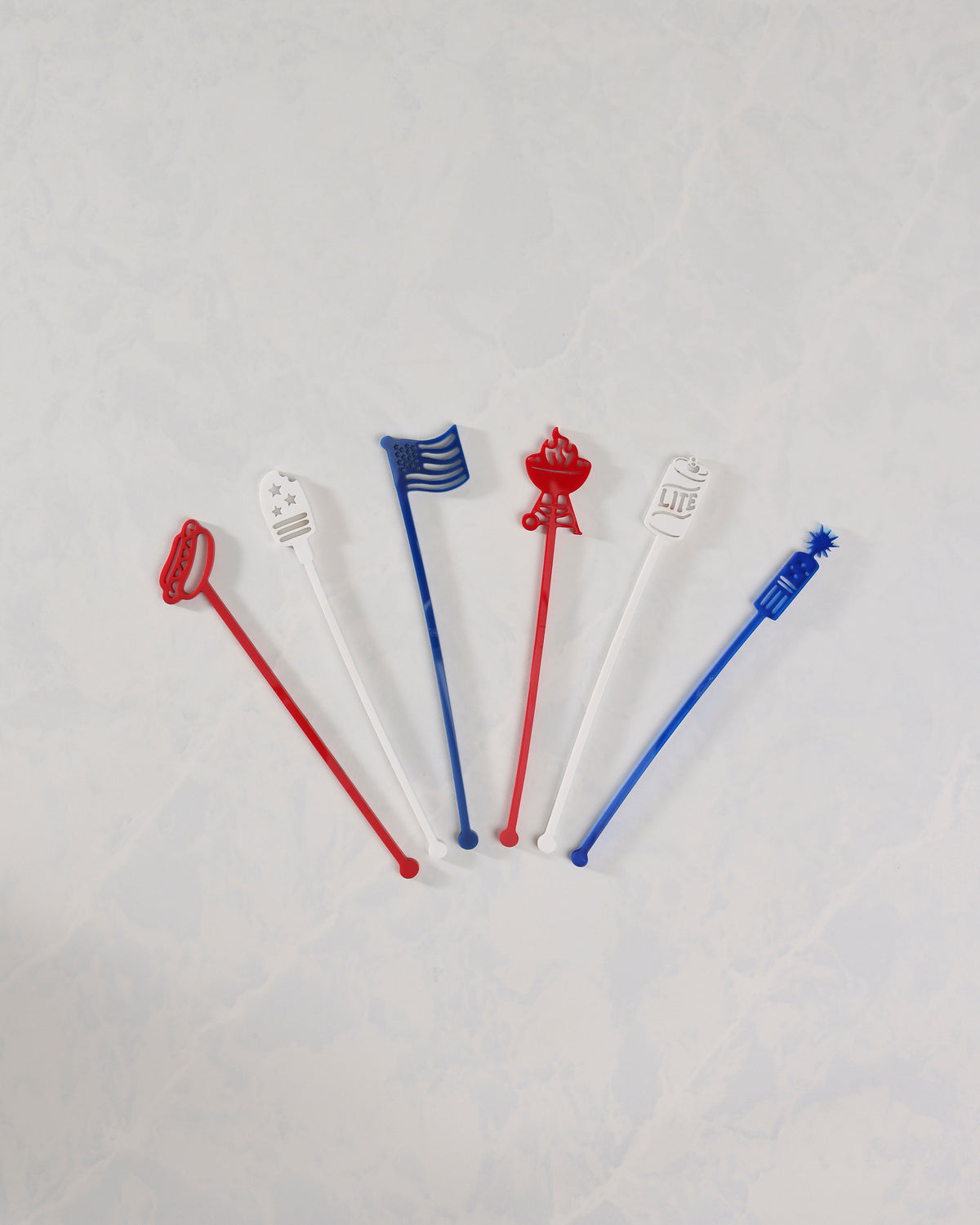 Six red, white, and blue July 4th stir sticks arranged separately on a white surface.