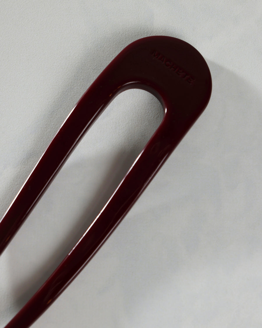 Close-up of the rounded end of the oxblood French hair pin with embossed branding.