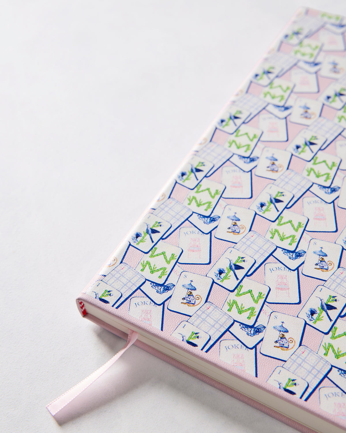 Angled close-up of the journal cover showing its repeating mahjong tile pattern, rounded binding, and pink ribbon bookmark.