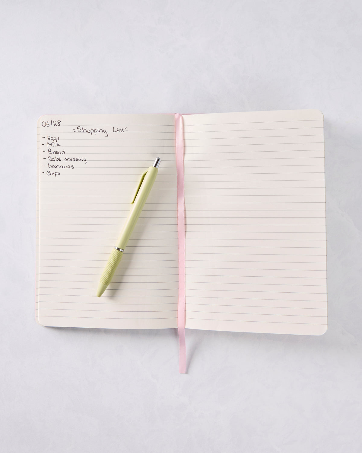 Open lined journal with a handwritten shopping list on the left page and a pale yellow pen across the pages.