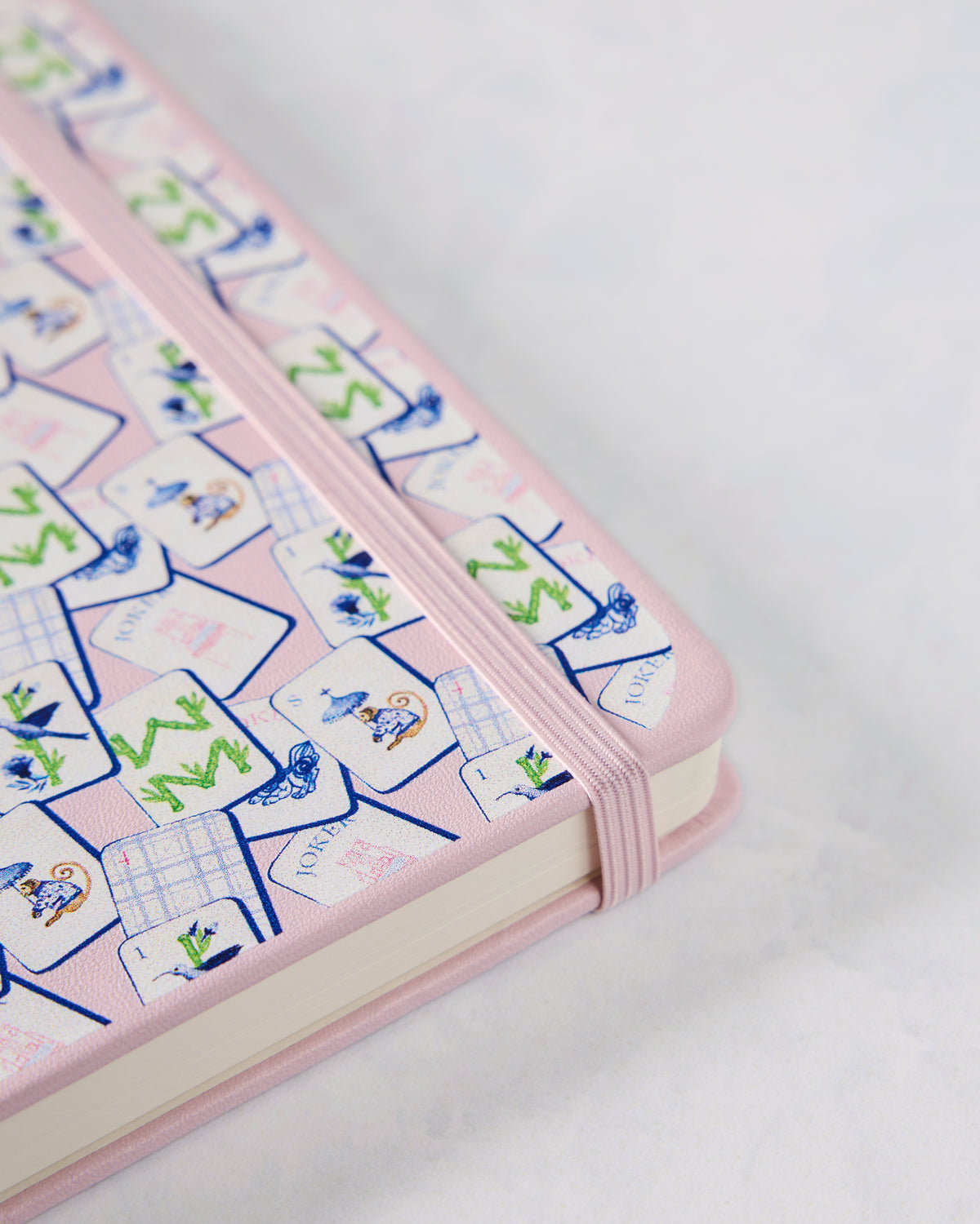Angled view of a pink mahjong-patterned journal with a matching elastic closure band.