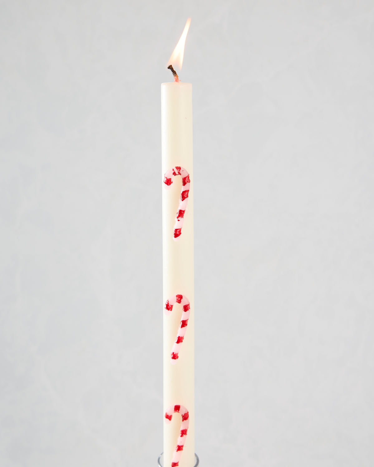 Lit white candle with pink and red candy-cane stripes.