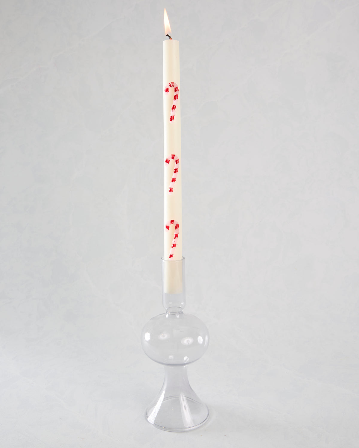 Lit white candy-cane-striped candle in a clear glass candle holder.
