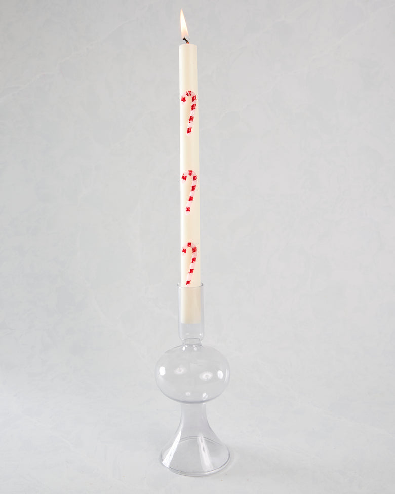 Lit white candy-cane-striped candle in a clear glass candle holder.