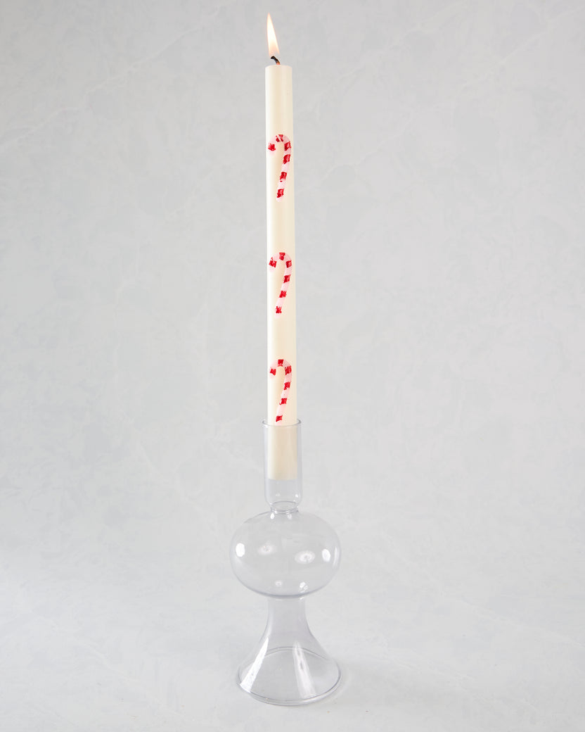 Lit white candy-cane-striped candle in a clear glass candle holder.