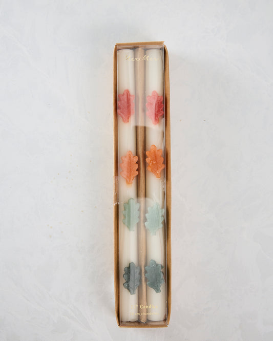 Boxed set of two white leaf-decorated table candles with pink, orange, pale green, and gray leaf accents.