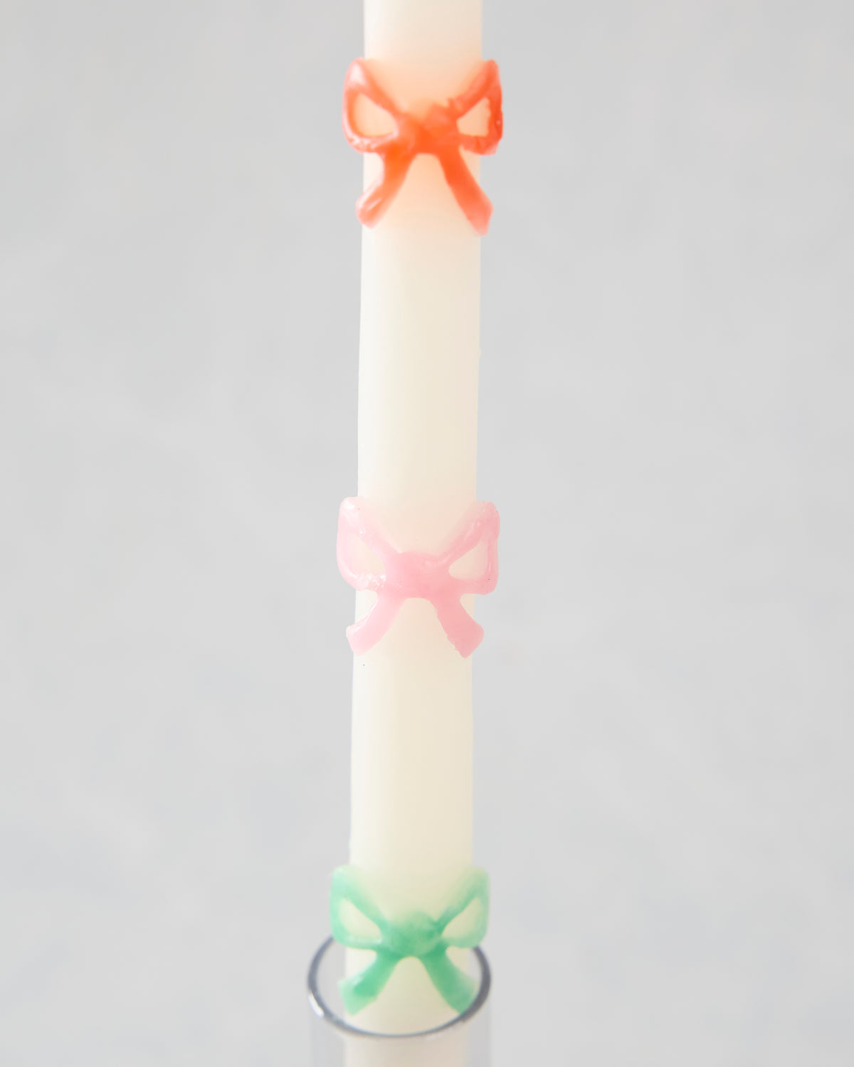 Close-up of a white taper candle with orange, pink, and green bow decorations above a candle holder.