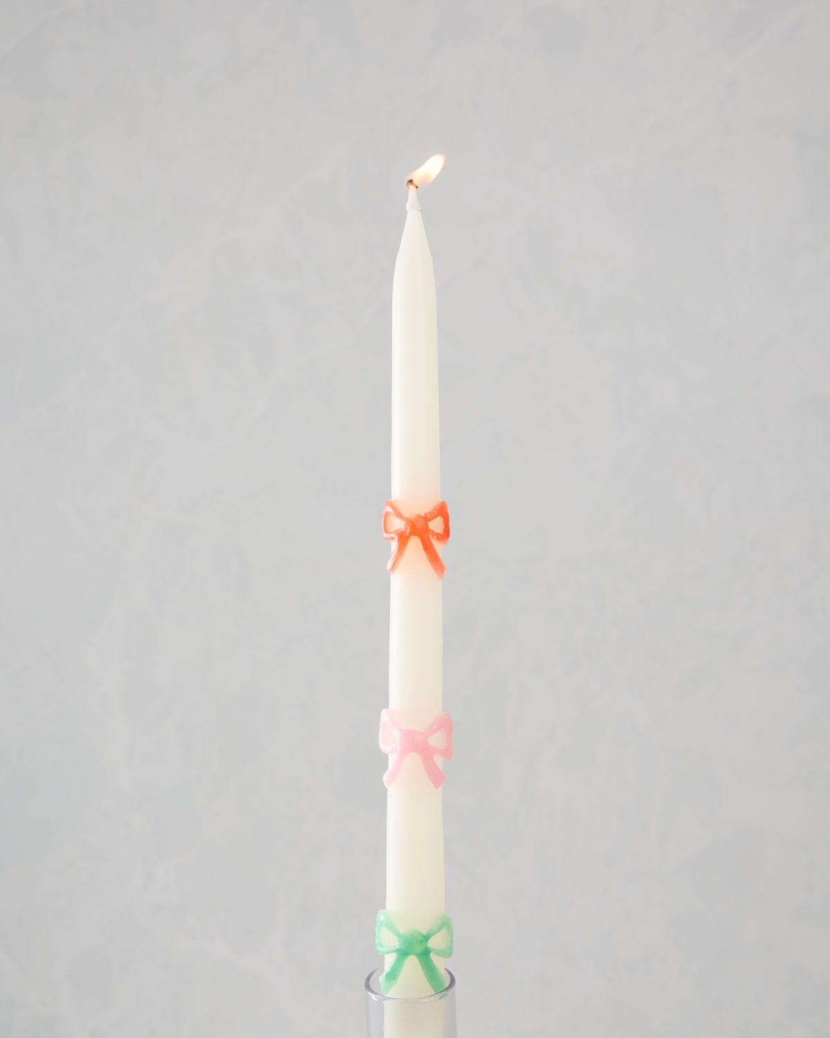 Lit white taper candle with orange, pink, and green bow decorations in a candle holder.