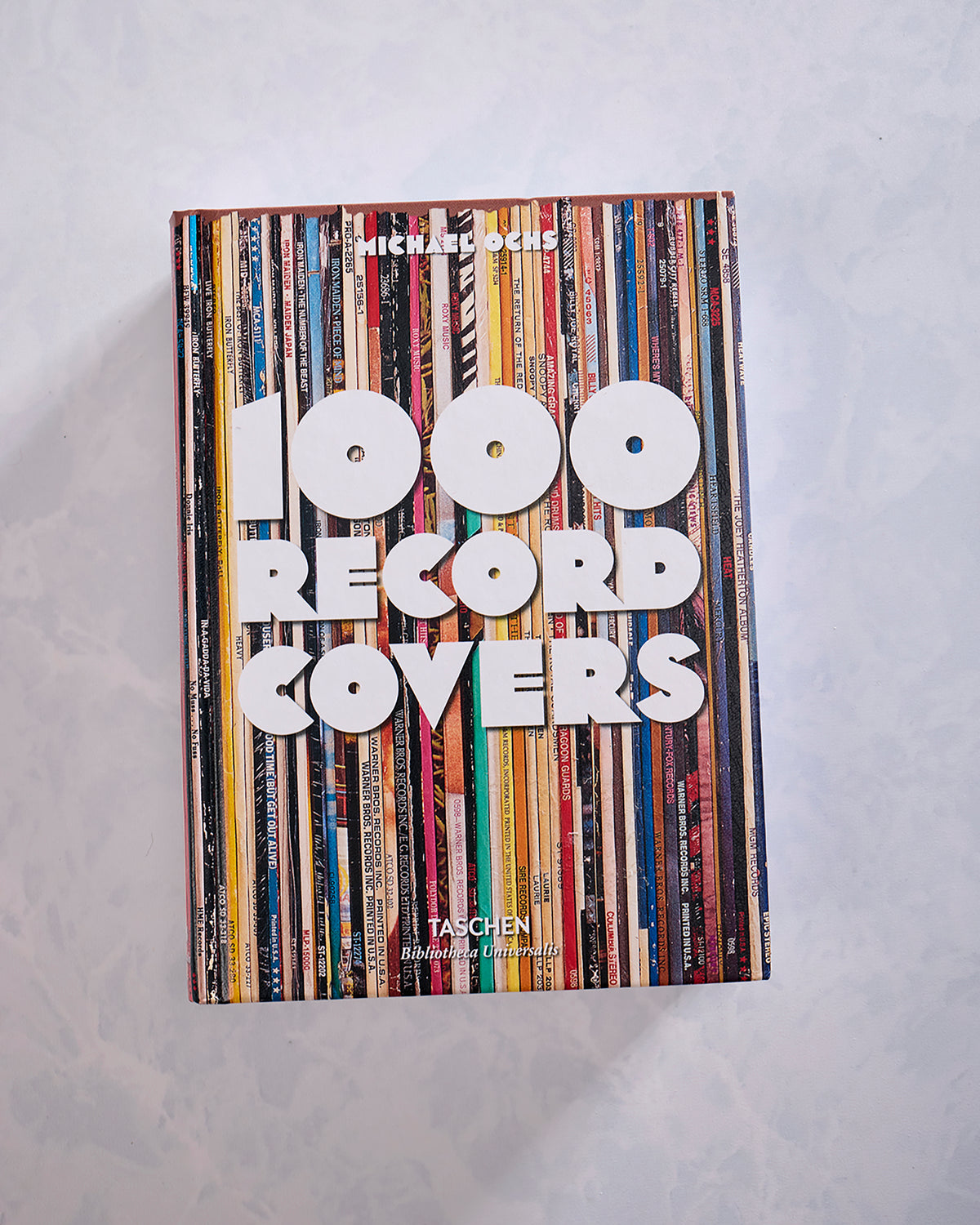 Front cover of 1000 Record Covers, featuring a collage of colorful record spines with large white lettering and three circular cutouts.