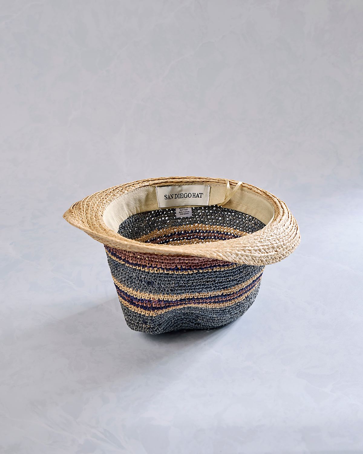 Three-quarter view of a crocheted fedora with a natural-colored brim and blue, navy, and tan striped crown.