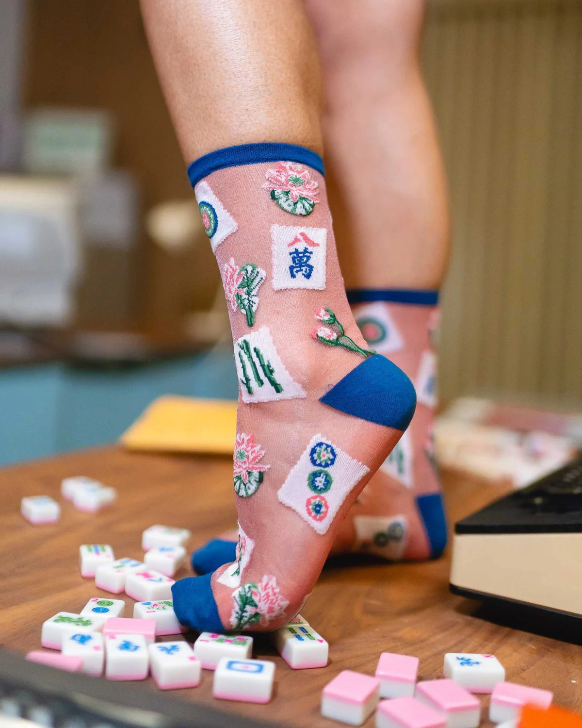 Close-up of sheer shimmer crew socks with colorful mahjong tile motifs and blue trim, worn with black tights.