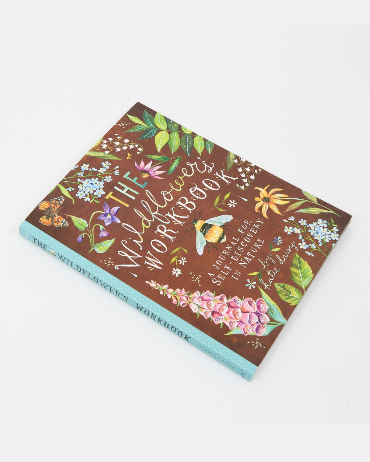 Angled view of The Wildflower's Workbook showing its illustrated floral cover and turquoise spine.