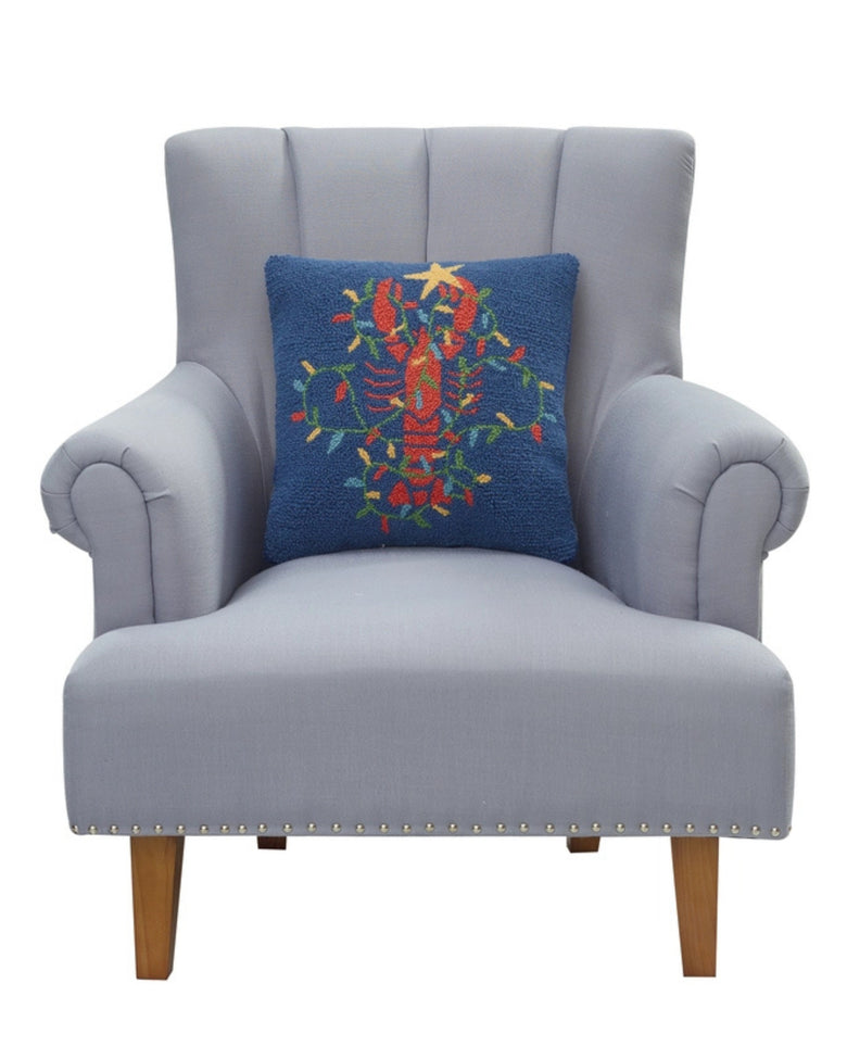 Navy lobster-design pillow shown resting against a light gray armchair.