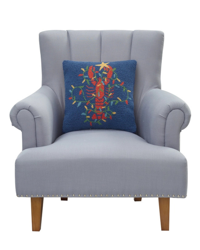 Navy lobster-design pillow shown resting against a light gray armchair.
