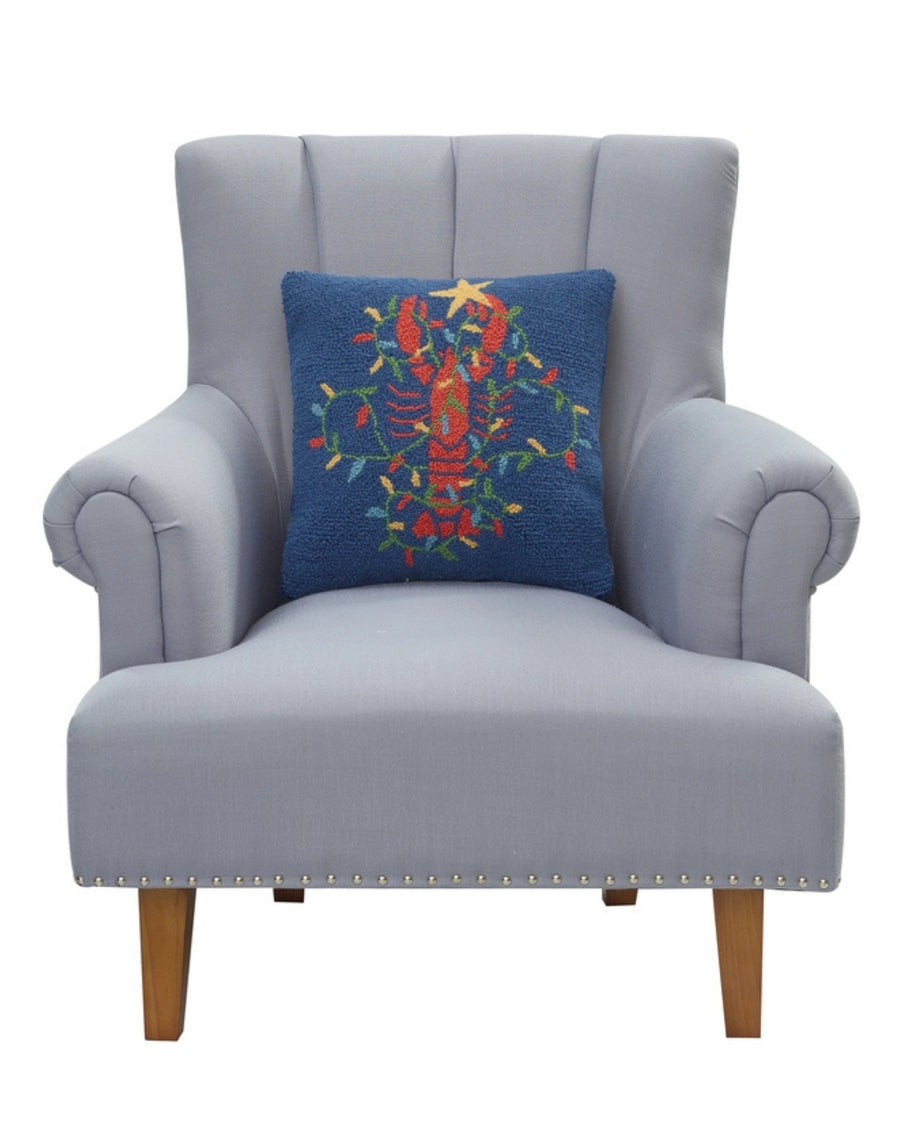 Navy lobster-design pillow shown resting against a light gray armchair.