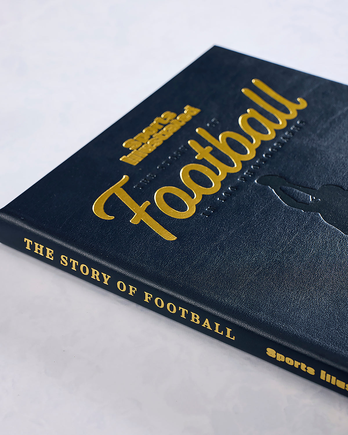 Angled close-up of the navy “The Story of Football” book cover and spine with gold lettering and a football player silhouette.