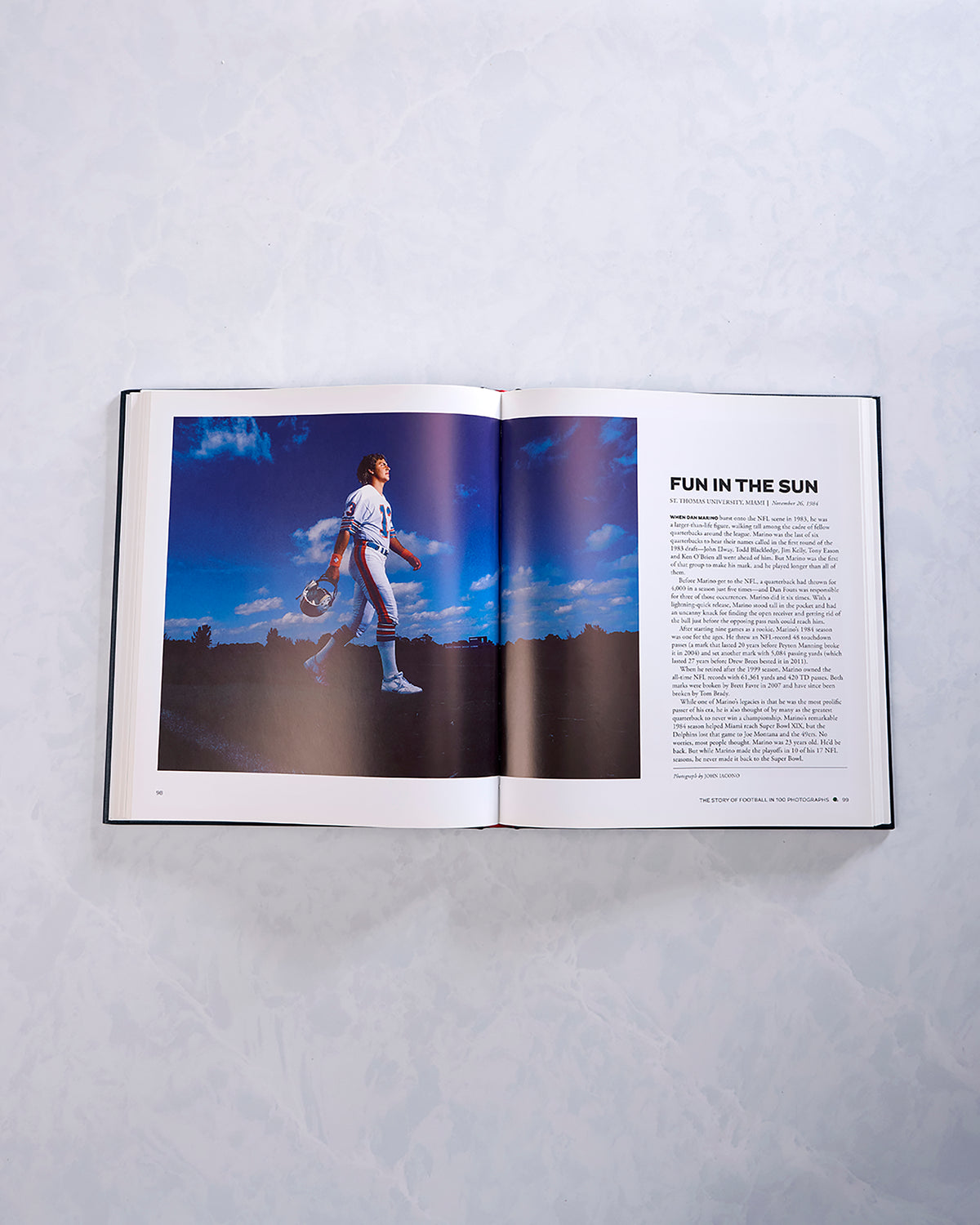 Open football history book showing a full-page photograph of a baseball player walking across a field beside the article “Fun in the Sun.”