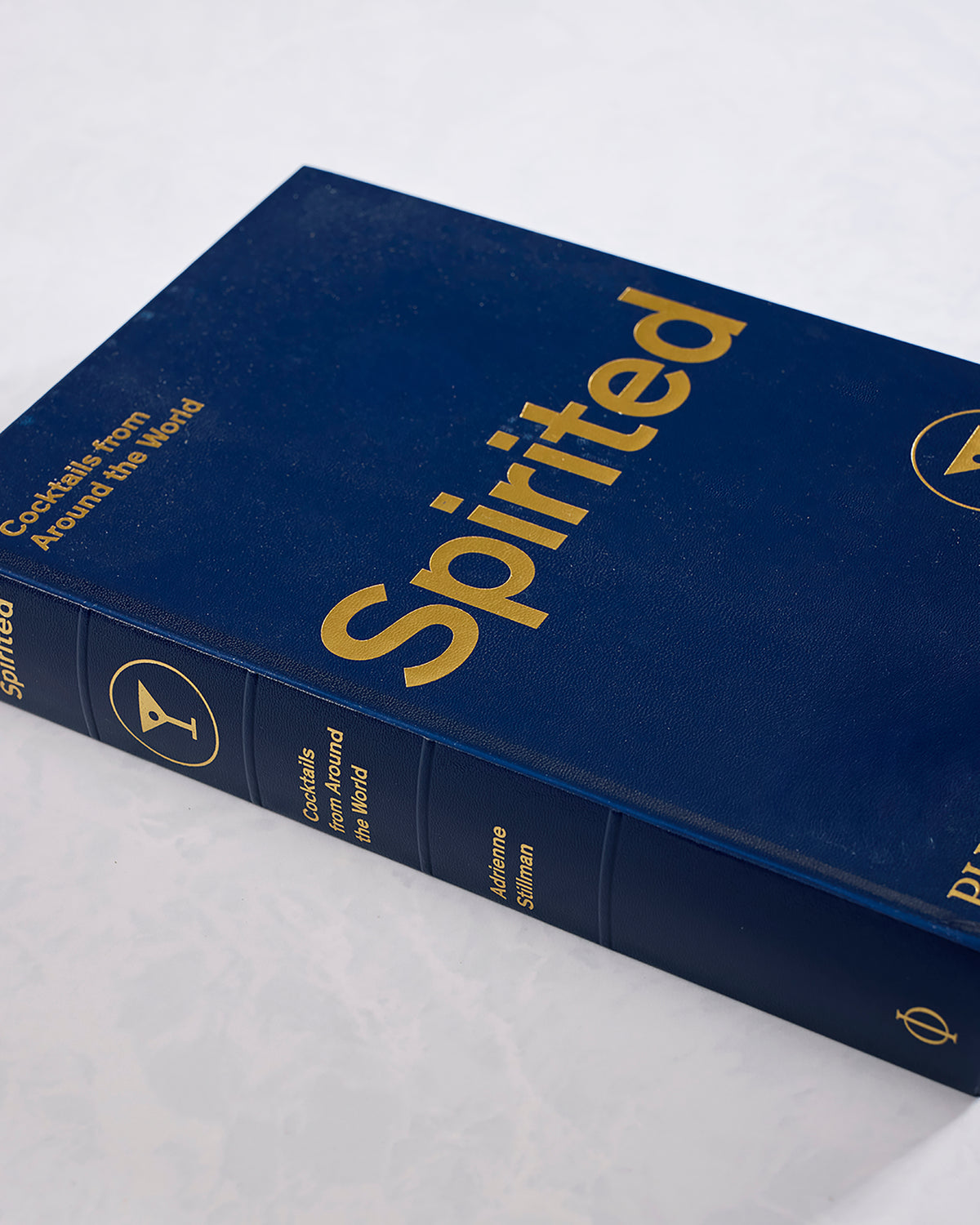 Angled view of the navy hardcover book Spirited: Cocktails from Around the World by Adrienne Stillman.
