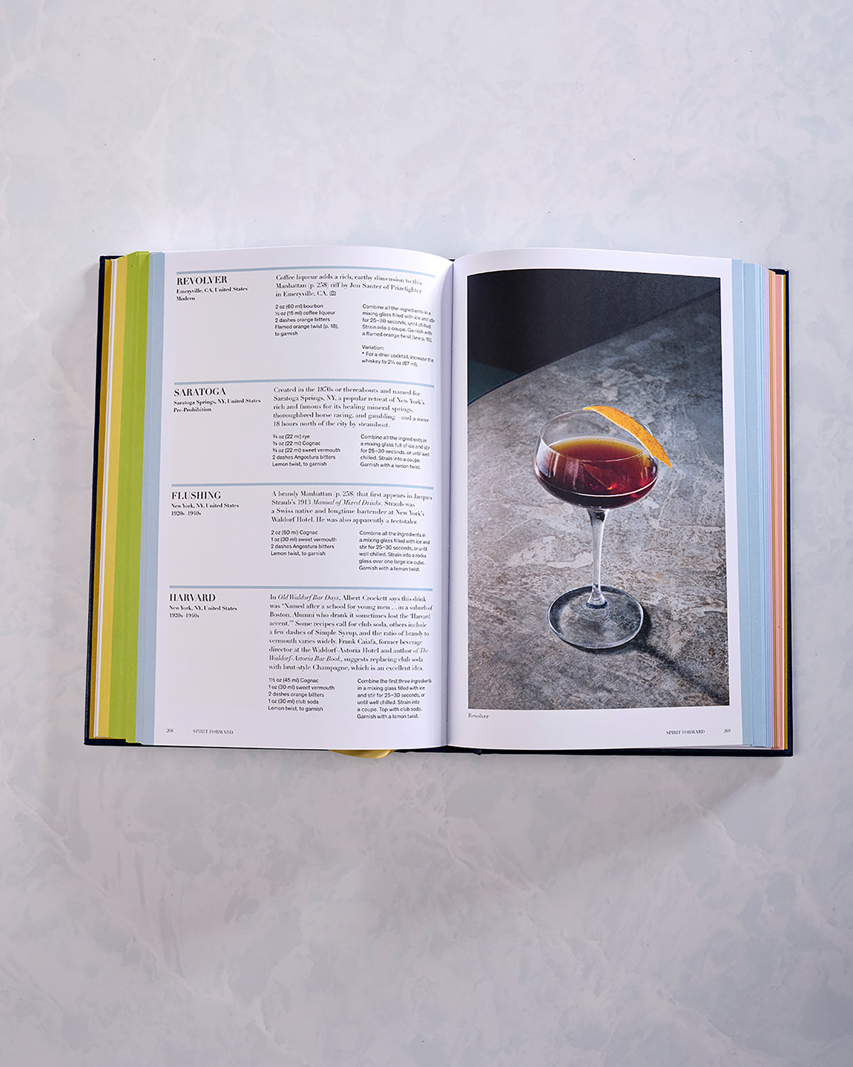 Open cocktail book spread with recipe entries on the left and a photograph of a cocktail in a coupe glass on the right.
