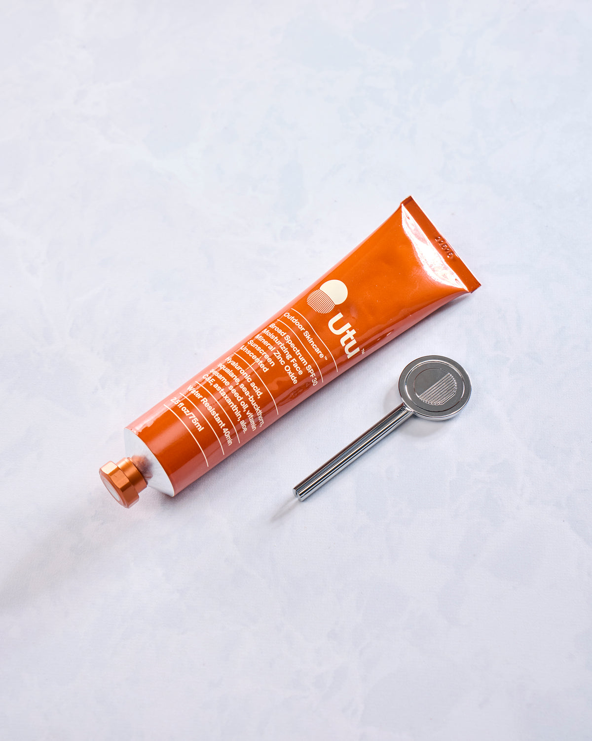 Orange Utu SPF 30 sunscreen tube lying beside a silver metal object.