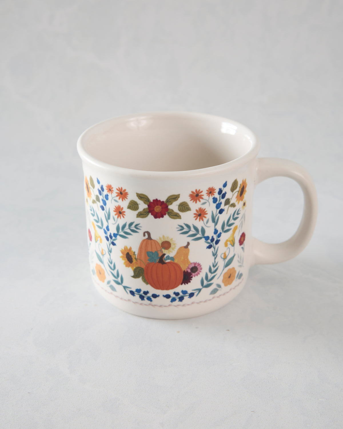 Front view of a white ceramic mug with pumpkins, flowers, leaves, and blue berry motifs.