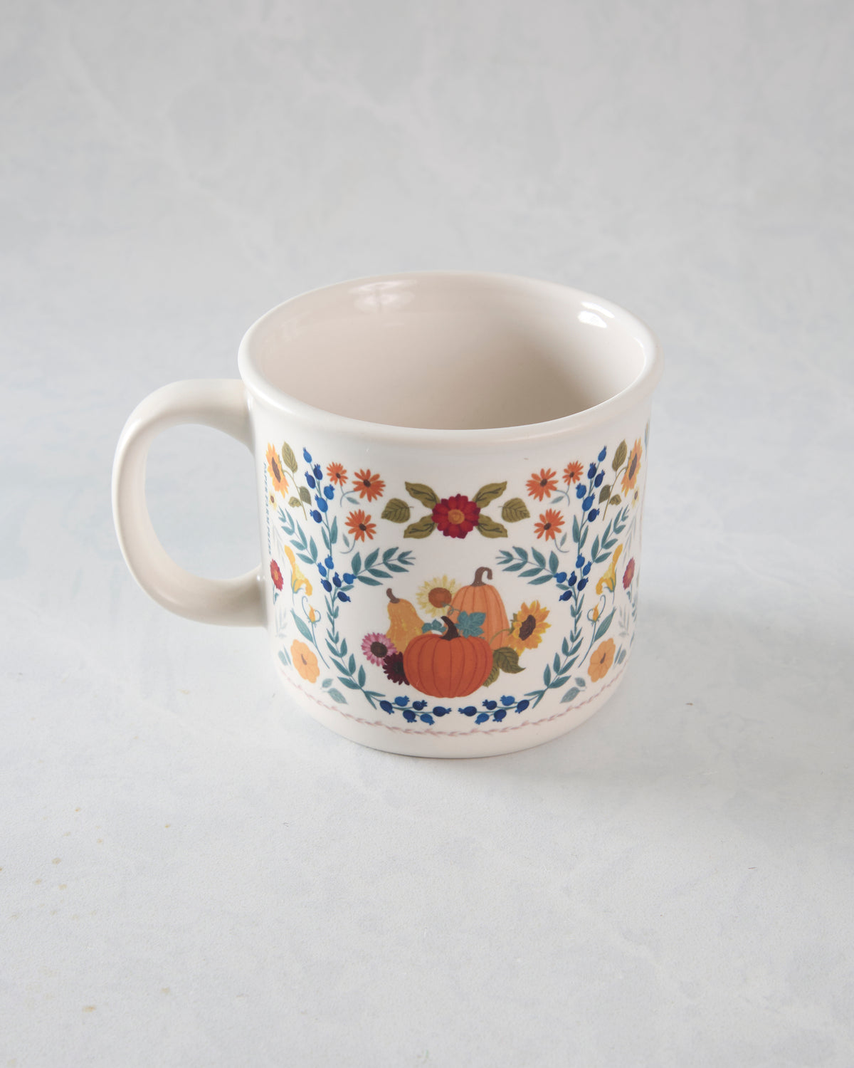 Angled view of the pumpkin and floral ceramic mug with the handle on the left.