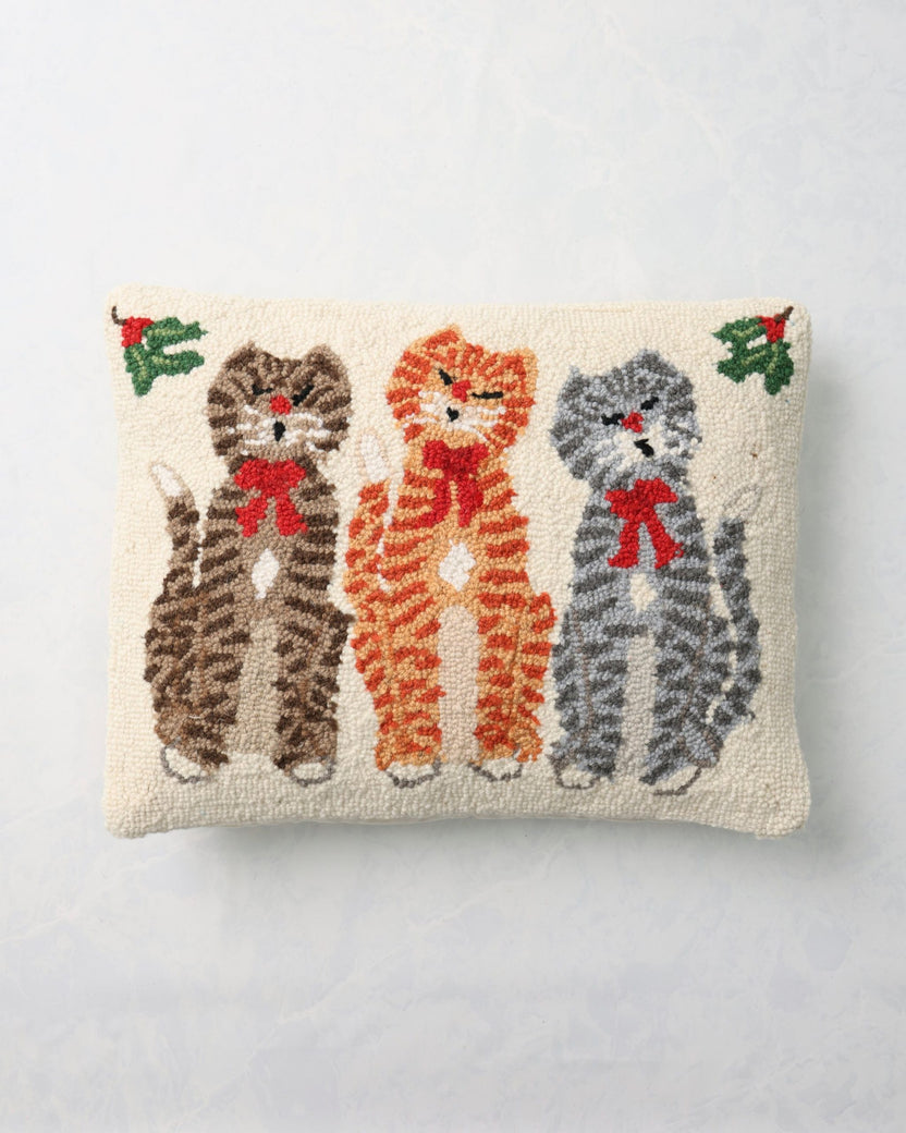 Front of a hooked pillow depicting three cats wearing red bows.