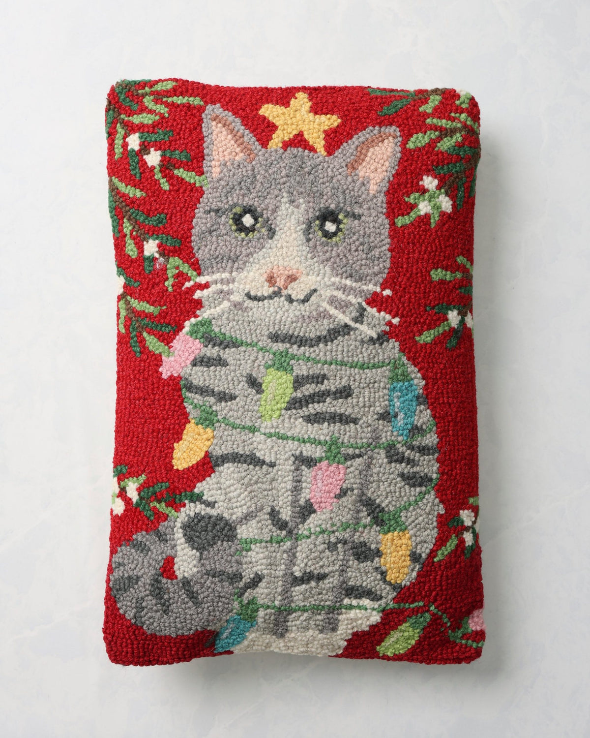 Front of a red hooked Christmas pillow featuring a gray cat wearing a star-topped holiday sweater.