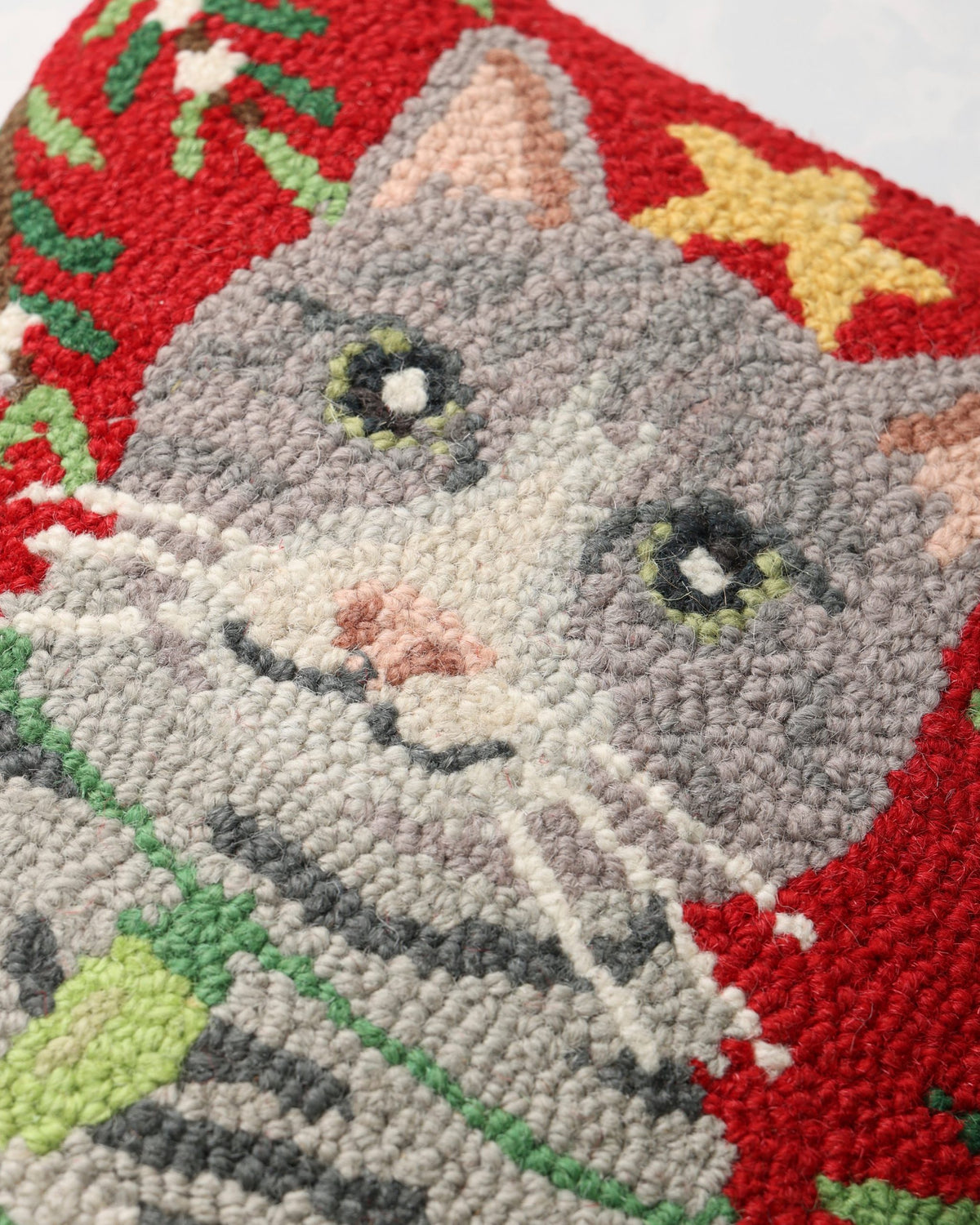 Close-up of the hooked gray cat design on the Christmas pillow, showing its face, star, and stitched texture.